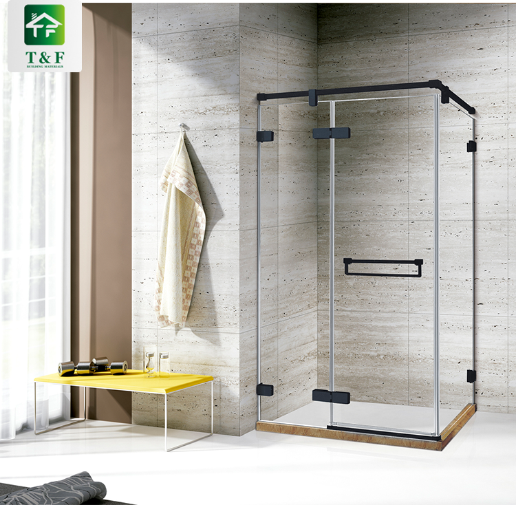 Buồng tắm kính góc vuông với khung viền đen, tường nền gạch xám, bàn vàng đặt bên cạnh.