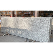 Tấm đá granite màu trắng xám, bề mặt nhám, đặt trên giá đỡ gỗ trong nhà kho.