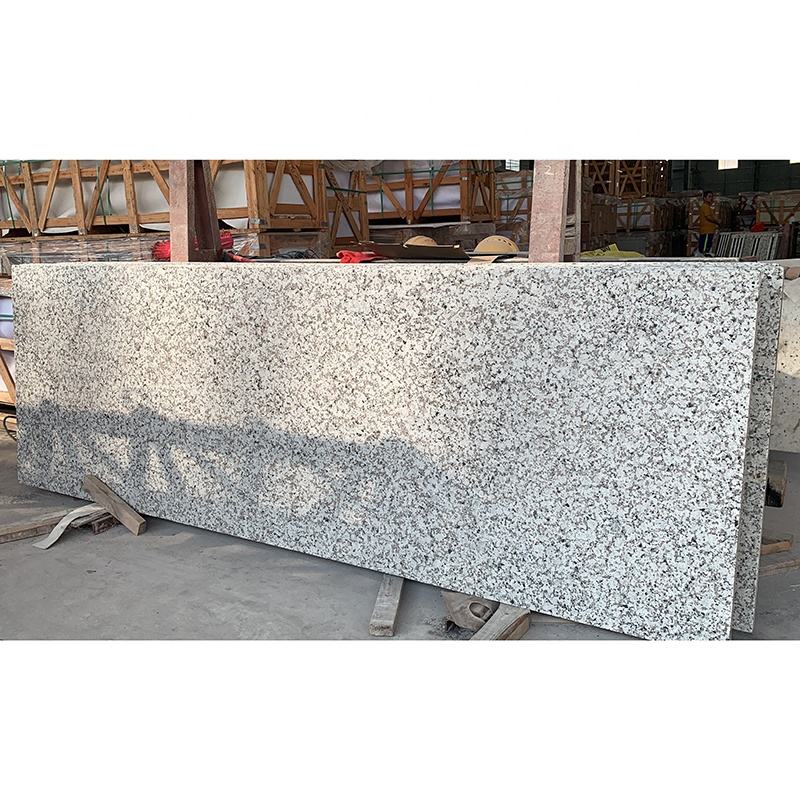 Tấm đá granite màu trắng xám, bề mặt nhám, đặt trên giá đỡ gỗ trong nhà kho.
