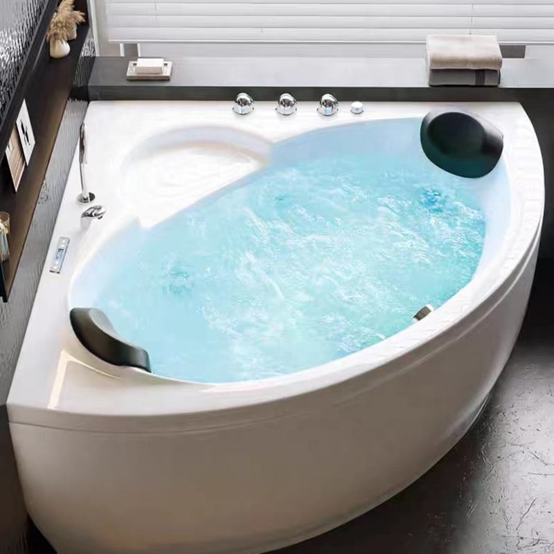 Bồn tắm góc trắng với nước xanh nhạt, hai gối đen và vòi sen kim loại.