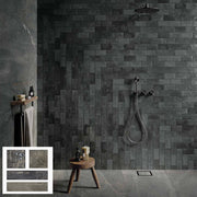 Phòng tắm tối giản với tường gạch xám đen, vòi hoa sen treo tường, kệ gỗ nhỏ và ghế đôn gỗ.