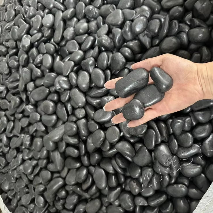 Bàn tay nắm các viên sỏi đen bóng, xung quanh là nhiều viên sỏi tương tự.