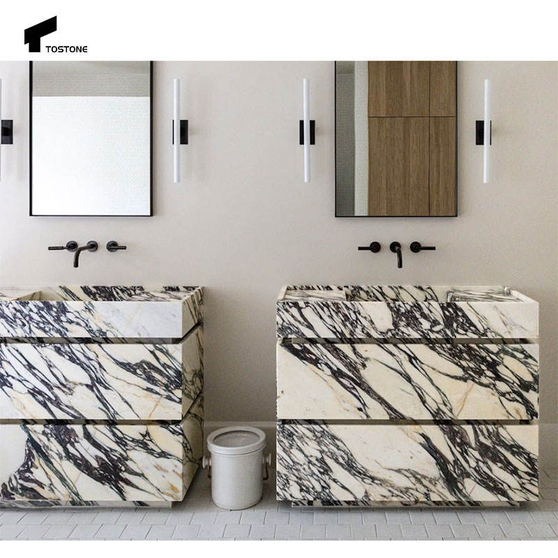 Hai bồn rửa đá cẩm thạch vân đen trắng, tường sơn nhạt, gương viền đen, đèn treo trắng.