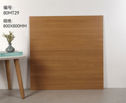 Tấm gỗ màu nâu nhạt 800x800mm dựa tường trắng, cạnh bàn có bình hoa và sách.