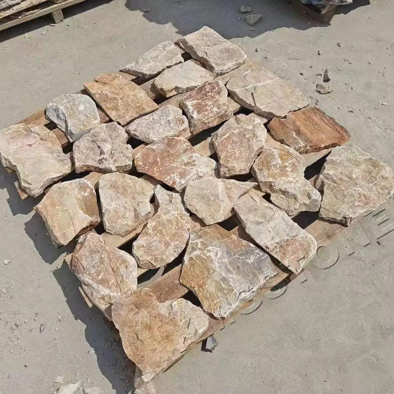 Các phiến đá màu nâu nhạt, xếp trên pallet gỗ, nằm trên nền đất xám.
