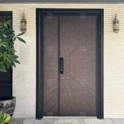 Cửa kim loại hoa văn tia sáng, hai đèn treo hai bên, tường gạch sáng, cây xanh bên trái.
