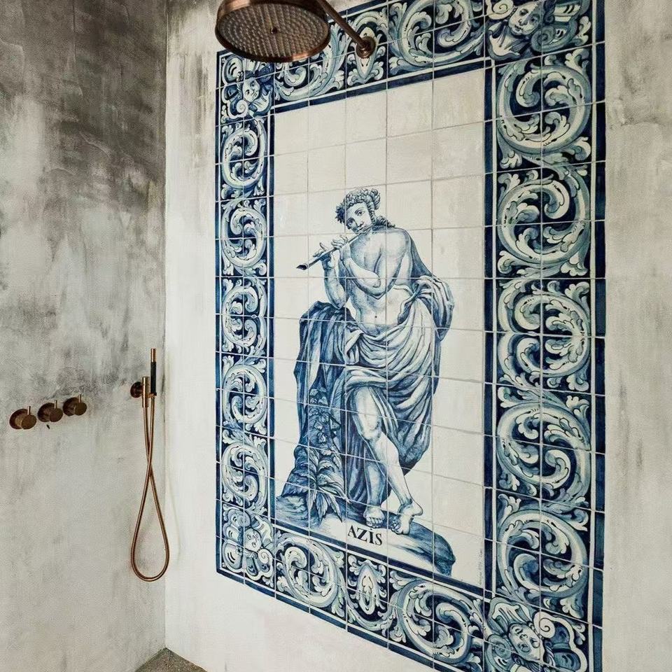 Tranh gạch men xanh-trắng, hình người thổi sáo, hoa văn uốn lượn, tường xám, vòi sen đồng.