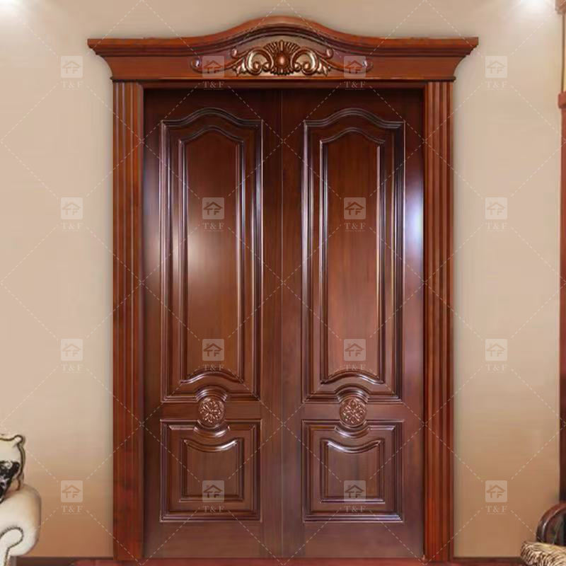 Cửa gỗ đôi màu nâu tối, chạm khắc hoa văn, tường màu be, ánh sáng chiếu từ trên.