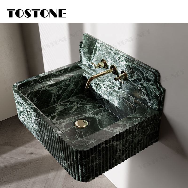Bồn rửa bằng đá cẩm thạch xanh đậm có vòi nước vàng nổi bật trên nền tường trắng.