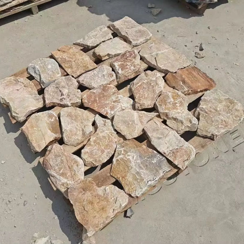 Các tảng đá lớn màu nâu nhạt nằm trên pallet gỗ, xếp thành hàng trên nền bê tông.