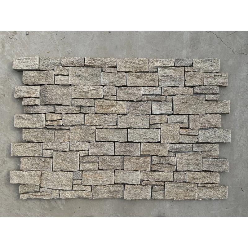 Bức tường gạch đá xếp chồng xen kẽ, màu xám, bề mặt thô ráp, nền xi măng.