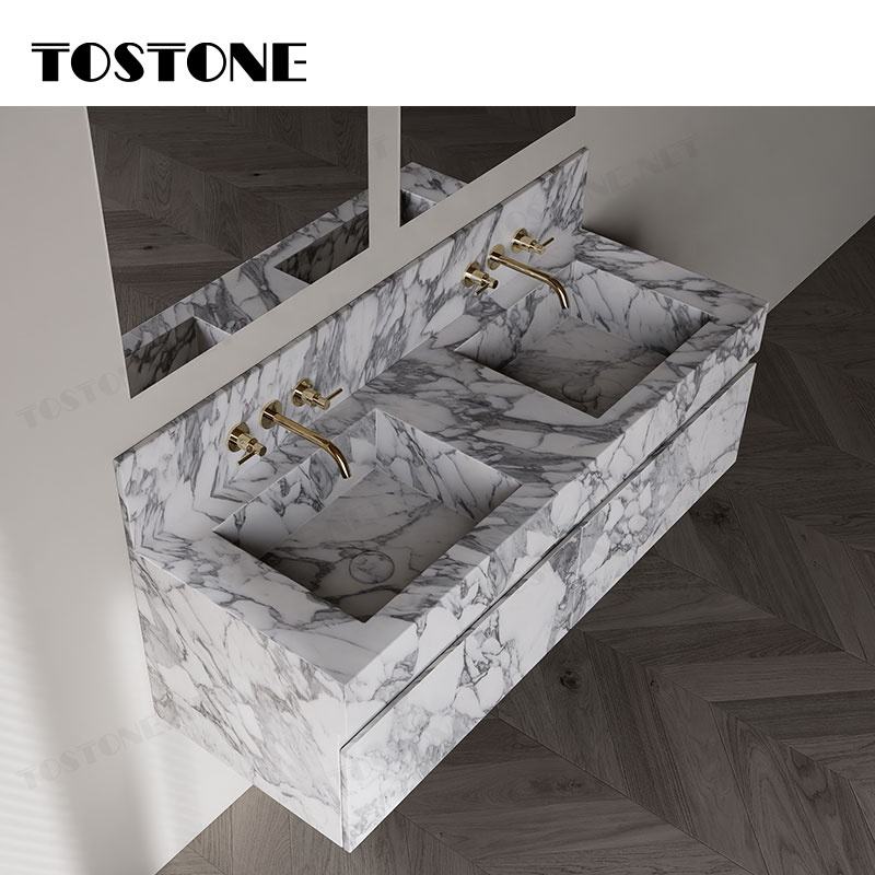 Bồn rửa đôi bằng đá hoa cương trắng xám, vòi nước màu vàng, nền gỗ nâu.