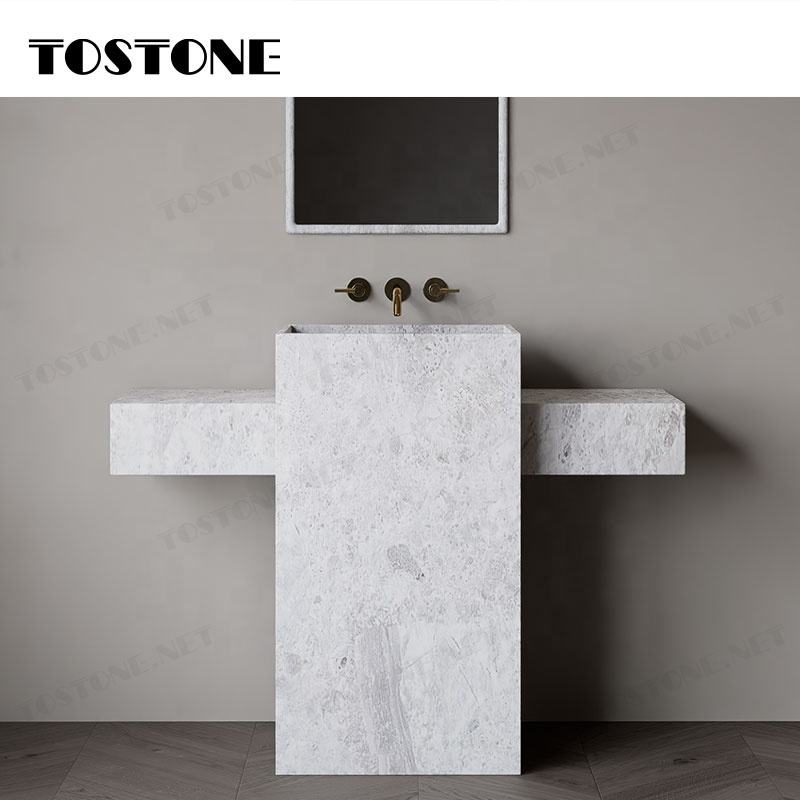 Bồn rửa mặt bằng đá trắng, vòi nước đồng, tường xám và gương hình chữ nhật phía trên.
