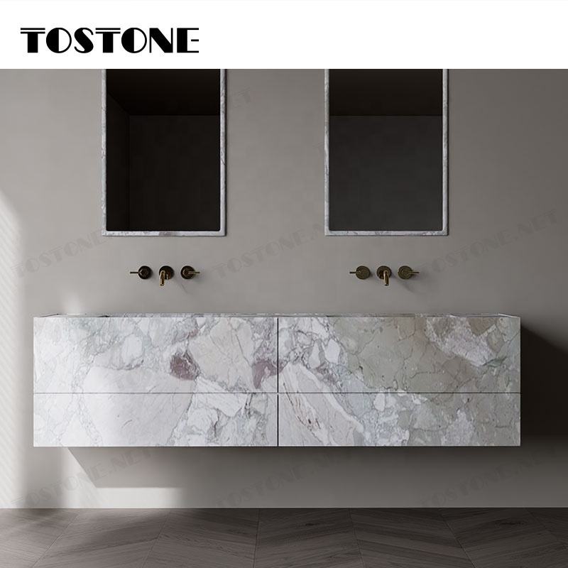 Bồn rửa đôi treo tường bằng đá cẩm thạch, vòi nước kim loại vàng, nền tường xám.