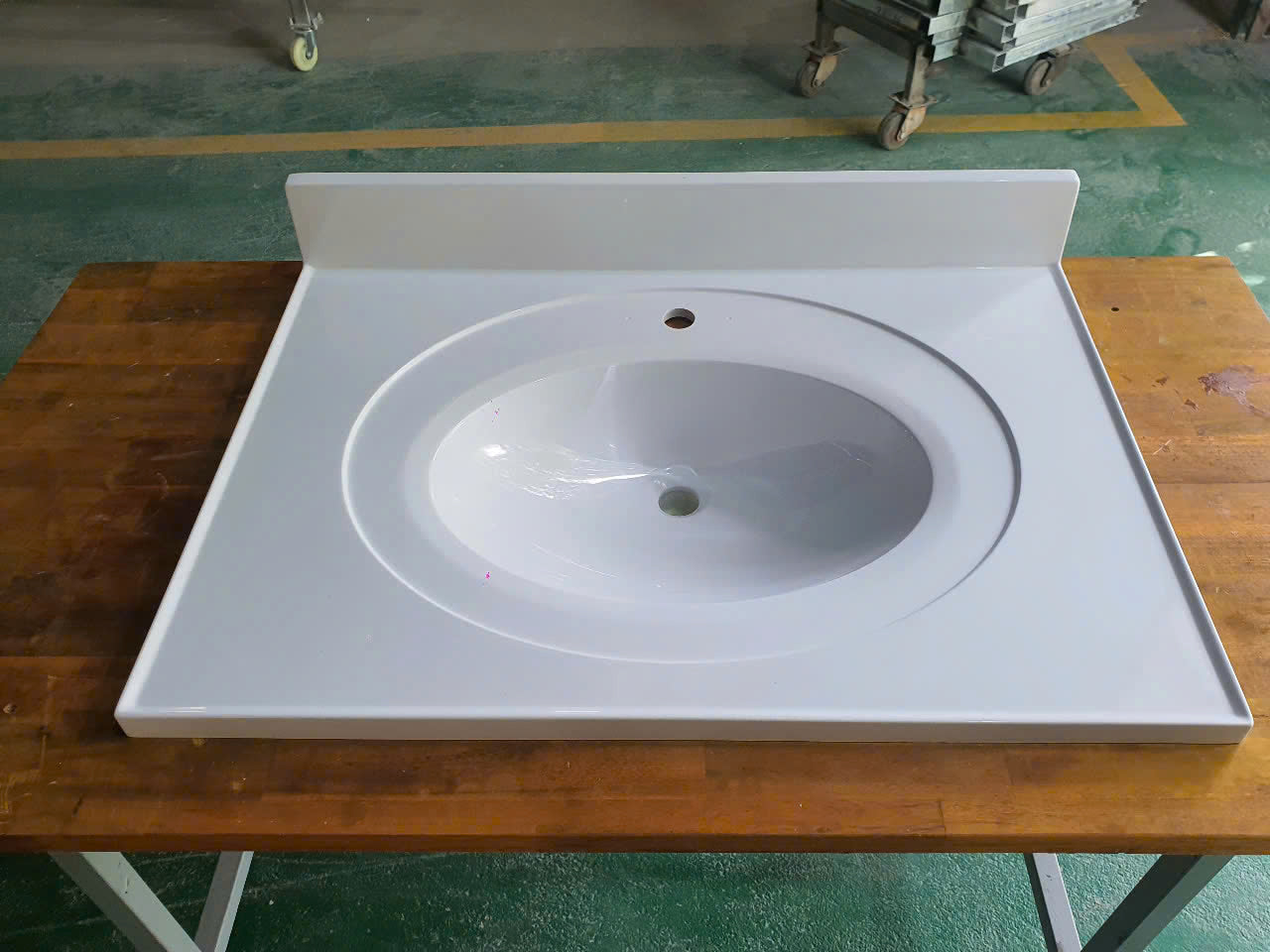 Chậu rửa mặt trắng hình bầu dục trên bàn gỗ nâu, có lỗ gắn vòi nước.