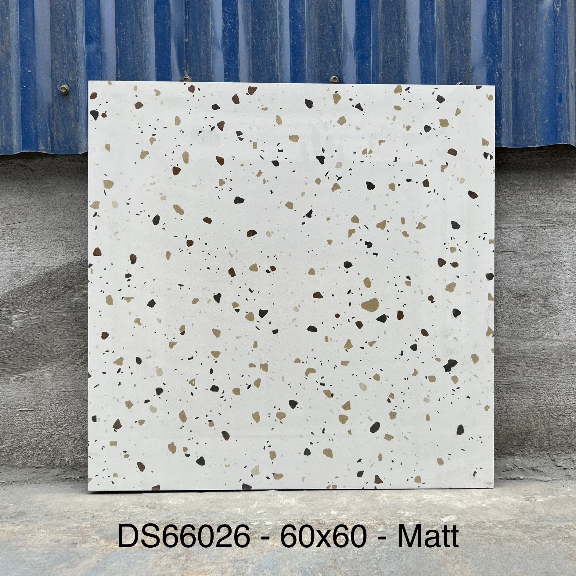 Gạch terrazzo màu trắng với họa tiết đốm nâu, đen và vàng, nền tường xanh xám.
