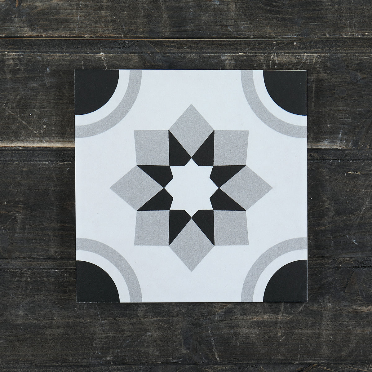 Gạch men họa tiết ngôi sao xám, đen và trắng trên nền gỗ tối màu.