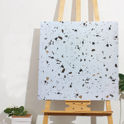 Khung tranh với họa tiết terrazzo đen, xám, nâu trên nền trắng, đặt trên giá vẽ gỗ.