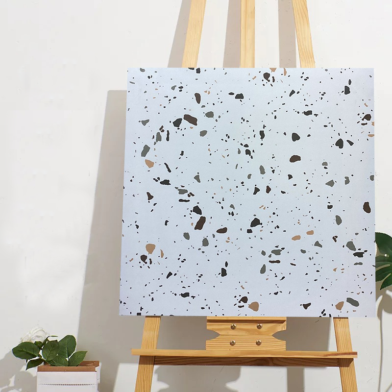 Khung tranh với họa tiết terrazzo đen, xám, nâu trên nền trắng, đặt trên giá vẽ gỗ.
