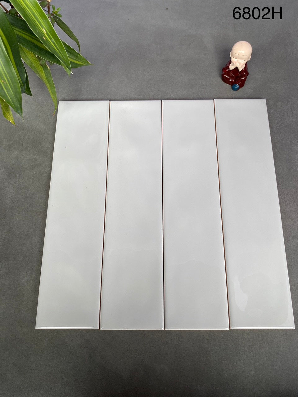Bốn viên gạch trắng xếp hàng trên nền xám, góc trái có lá cây xanh, góc phải có tượng nhỏ.