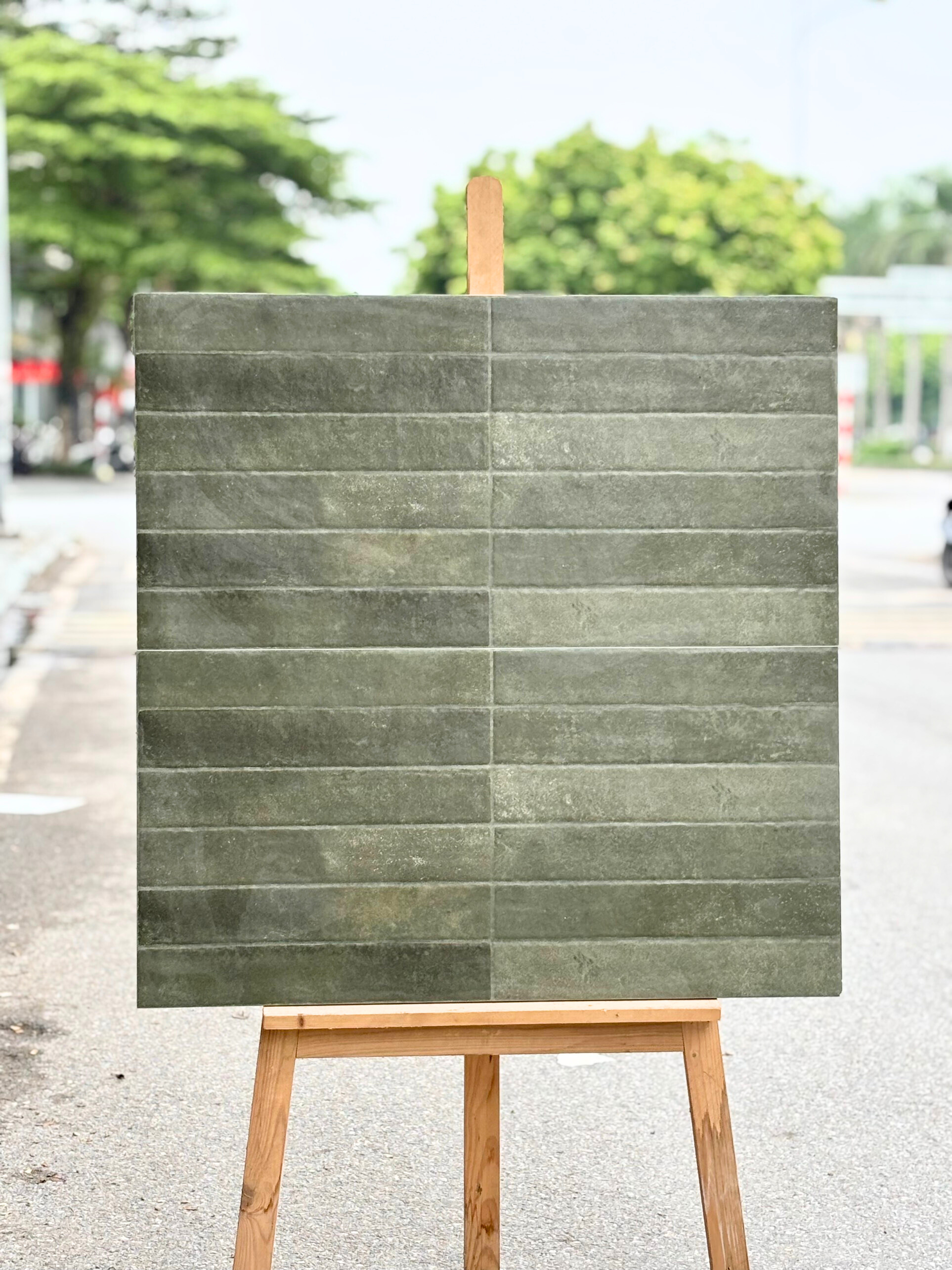 Bảng gạch màu xám xanh đặt trên giá gỗ, nền là cảnh đường phố và cây xanh.